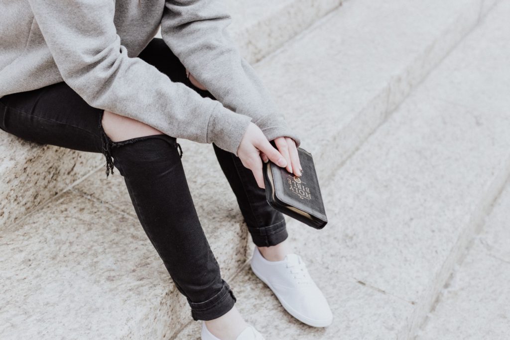 Young adult seated on steps outdoors holding a Bible illustrating the part played by Scripture and faith in mental and emotional health.